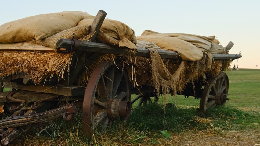 Rustic wooden cart with burlap sacks and straw on field in rural landscape