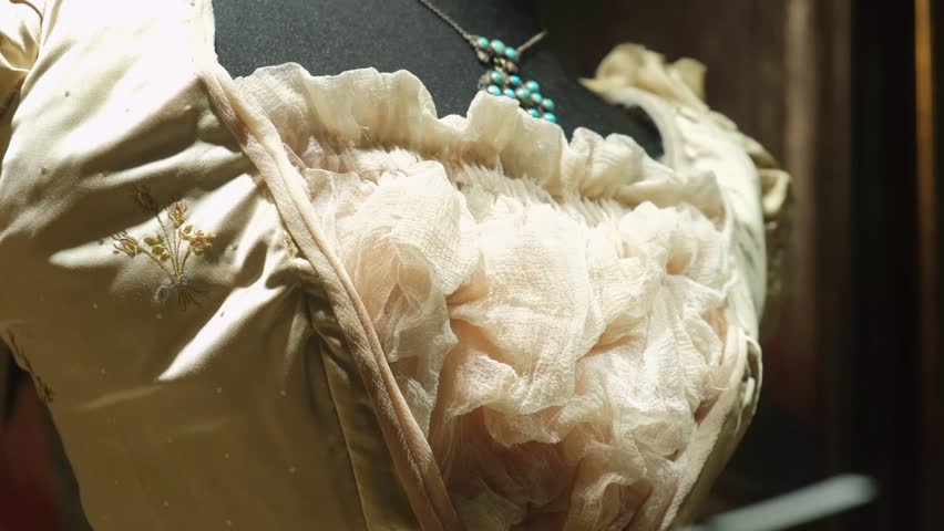 Close-Up of an Elegant Vintage Dress with Intricate Embroidery and Delicate Ruffles Displayed on a Mannequin, Highlighting Fine Fabric Details and a Complementary Necklace