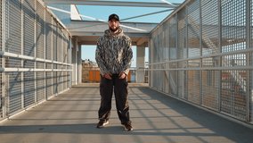 Energy young dancer male in zebra-patterned hoodie and beanie performs an energetic dance move on urban bridge at sunset. Industrial setting sunlight create dynamic, modern atmosphere. Lifestyle - Powered by Shutterstock - Get 15% off with code: PIKWIZARD15