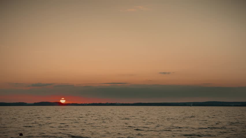 Orange sunset over water with distant coastline and clouds