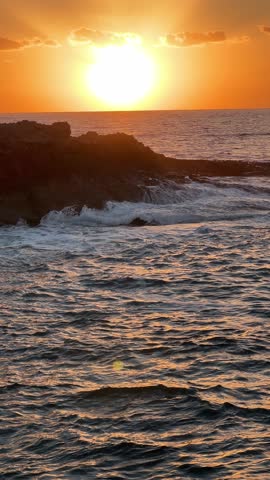 Sunset on Kissonerga beach in Paphos district of Cyprus on the Mediterranean Sea. The movement of sea waves against the background of the sunset.