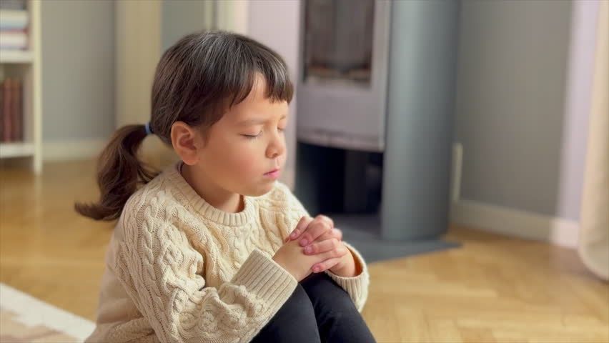 Little girl with her eyes closed praying sitting on the floor of her house