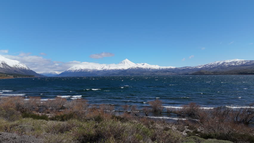 Turquoise waves of Huechulafquen lake breaking on shore with Lanin volcano in background. Patagonia, Neuquén, Argentina