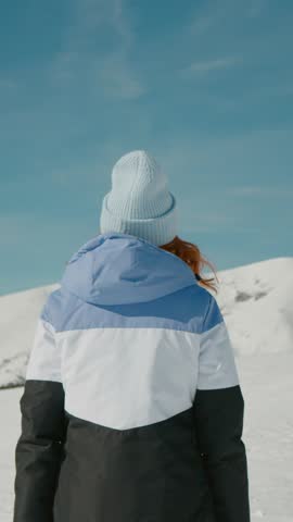 Vertical Screen: Winter lover woman turns to the camera and smiles. Adventurous tourist facing the beauty of the snowy mountain peaks. Travelling and exploring concept.