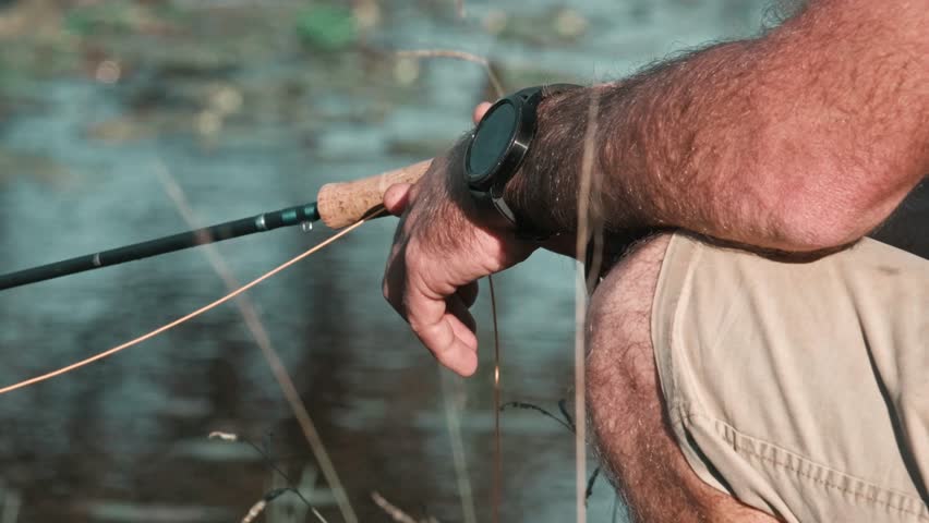 Fisherman reeling in his line while fishing by. a lake