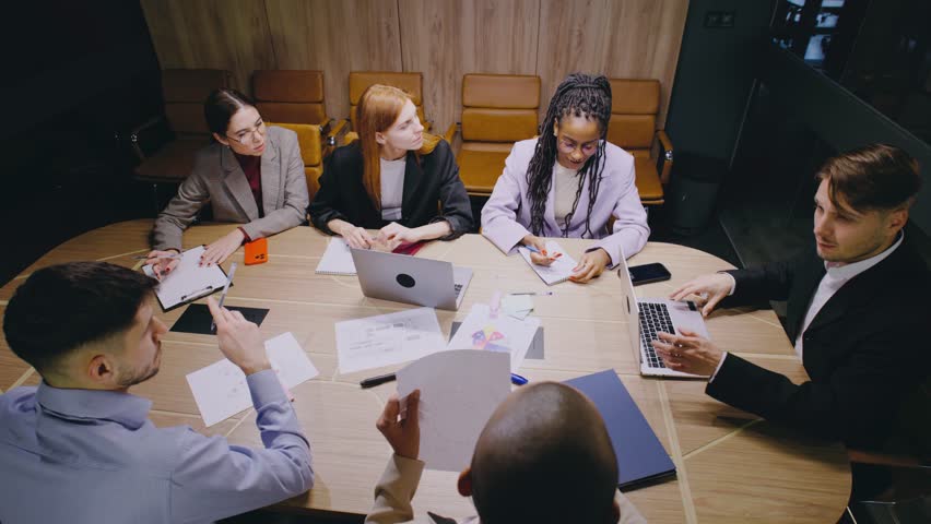 A diverse group of professionals collaborates in a business meeting, engaging in analysis and brainstorming to achieve shared goals. They contribute ideas, take notes, and plan projects