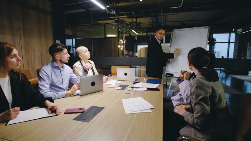 A team meeting is taking place in a contemporary, modern office environment, featuring a presentation that involves collaboration, discussion, and brainstorming among participants