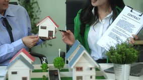 Two young Asian businesswomen discuss housing estate project at desk in modern office, net-zero waste management, clean energy, recycling, and renewable solutions with models and contracts. - Powered by Shutterstock - Get 15% off with code: PIKWIZARD15
