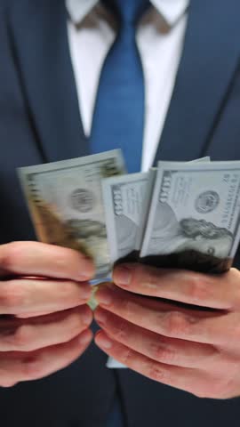 Formally dressed man is counting US Dollar bills, close-up.