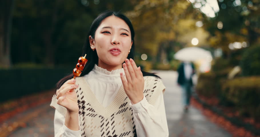Street food, eating and happy with Japanese woman in park for dessert, traditional cuisine and holiday. Dango, taste and festival season with asian person and culture snack for sweets and lunch