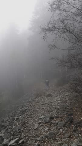 Hiker is walking on a rocky path through a foggy forest in Chamonix, France in November