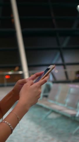 Vertical, A person browsing a smartphone at modern airport. Background includes airport interiors, showcasing travel and technology. Perfect for tech or transportation topics.