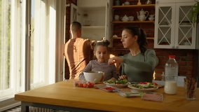 Family shares laughter while preparing healthy breakfast in modern kitchen. Parents and daughter gather around wooden table with fresh salads and ingredients. - Powered by Shutterstock - Get 15% off with code: PIKWIZARD15