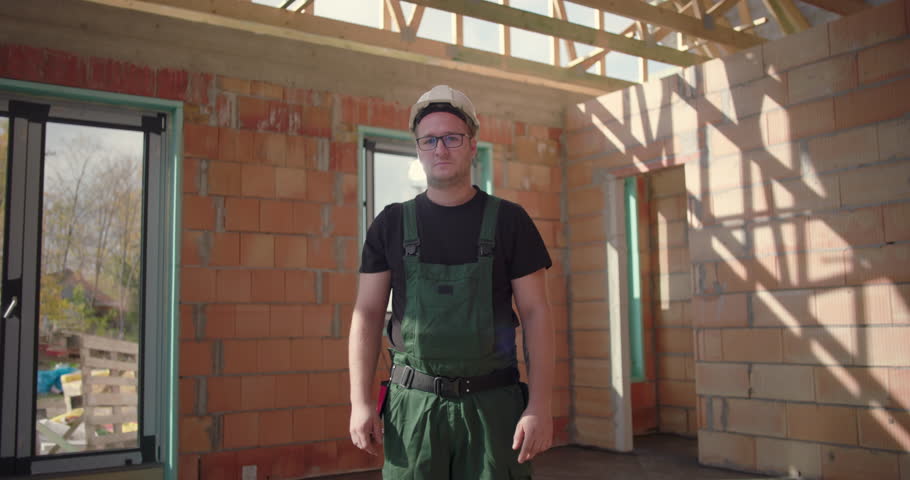 Close-up of construction worker in hard hat and glasses, standing inside an unfinished building, looking serious and dedicated, representing precision and work focus