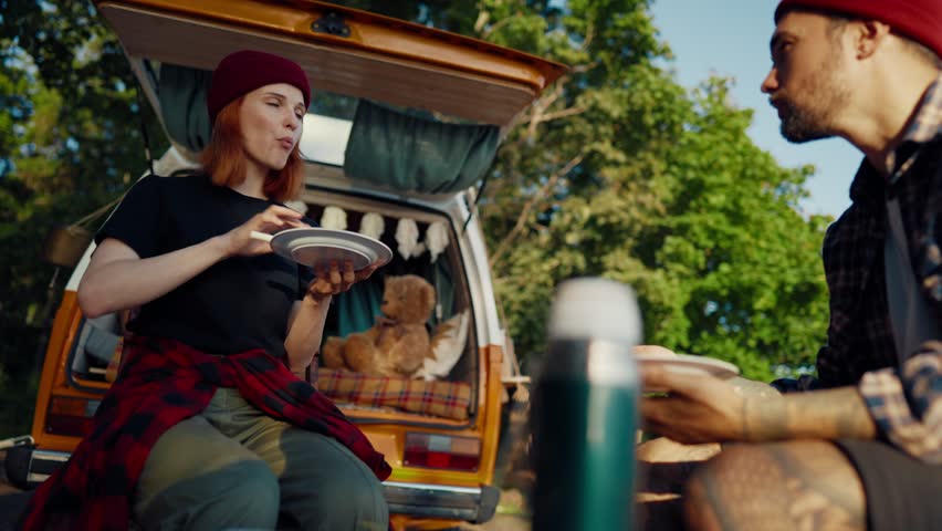 Breakfast in nature, woman and man traveling by motorhome together in weekend. Portrait of joyful lady eating tasty meals, merry joint time of honeymooners and lovers, trip by camper van in forest