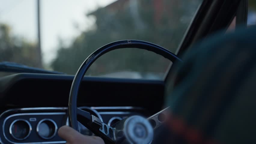 Man driving classic convertible vintage car steering wheel down a sunny road. Sun shining in early morning or afternoon as male driver holds the vintage steering wheel. Right hand car in Australia