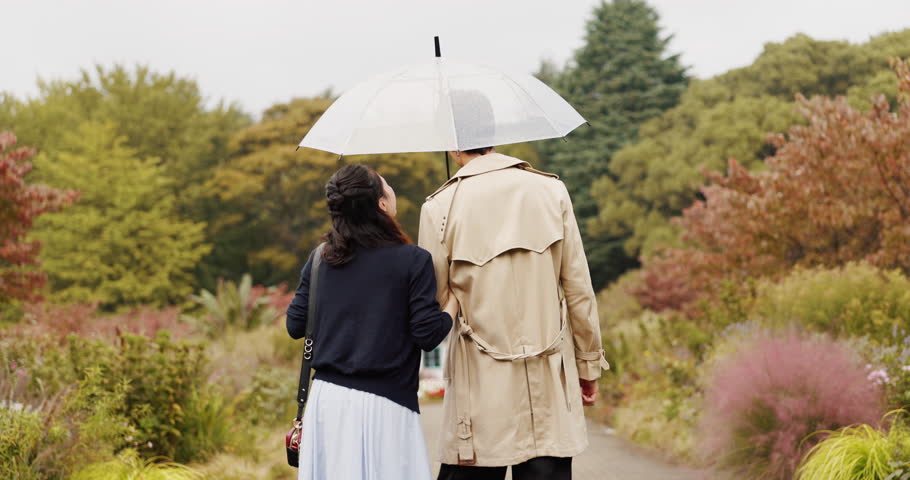 Park, umbrella and back of Asian couple in rain walking for commute, journey or travel outdoors. Dating, autumn and man and woman for bonding, talking or love with protection from weather in Japan