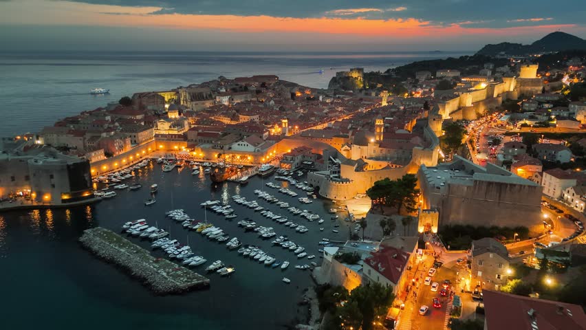 Sunset over Dubrovnik, Croatia. Vibrant marina filled with boats and illuminated city walls. Aerial evening shot of Dubrovnik. 4K HDR