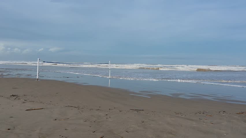 Long waves hitting the beach after a storm, a volleyball net submerged in water, and a dark, cloudy sky above.