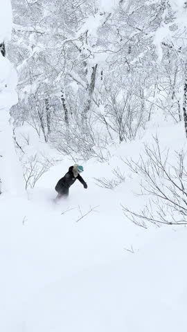 VERTICAL, POV: Skilled woman snowboarding through fresh powder and spraying snow in a white forest. Adrenaline winter adventures and playful snowboard riding in the freshly snowed Japanese mountains.