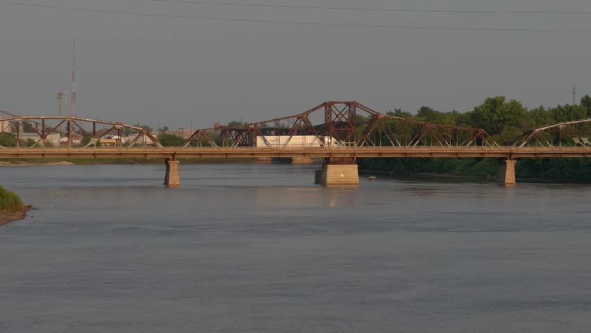Cityscape, red river in Winnipeg, Manitoba, summer, warm evening, bridge for cars in the distance. A large truck crosses the bridge. Big river at sunset with blue water.
