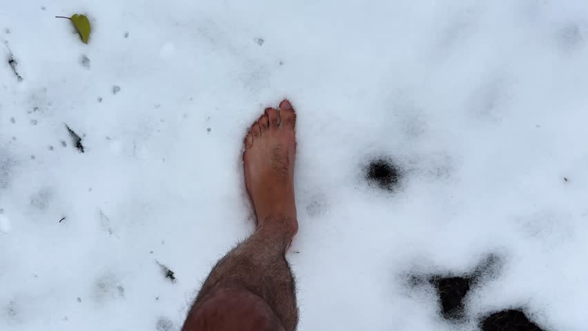 Top view of male bare feet stepping on white snow. Legs of man going on snowy trail. Young guy hardening at cold winter. Concept of healthy lifestyle. POV Slow motion