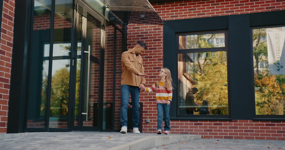 Front camera view of handsome Caucasian man talking with his small daughter. Male showing size of something with one hand. Pointing at object off camera with one finger. Child smiling with joy.