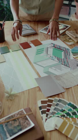 Vertical high angle view of two unrecognisable coworkers developing interior design of house using colour palettes and samples of materials on wooden table
