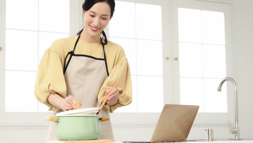 Woman cooking in the kitchen while looking at a laptop