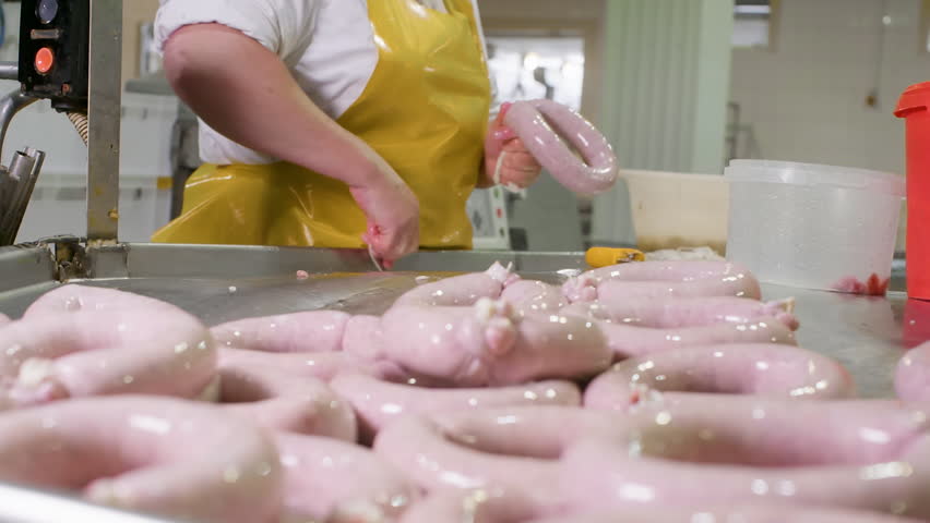 Close-up of a butcher arranging fresh sausages on a metal table, showcasing the sausage production process in a meat processing facility