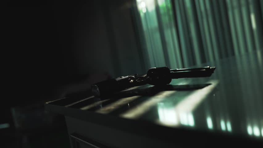 Close up man hand taking revolver gun from the table shoots and put back. Backlight by dramatic sunlight through the window blinds. Cinematic crime scene suicide or murder concept.
