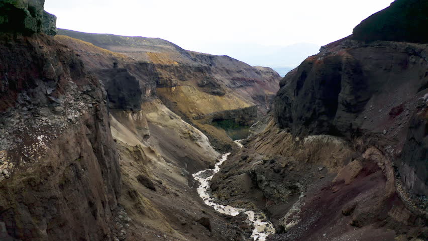 A dramatic aerial view of a steep canyon carved by a small stream, surrounded by layered volcanic rock formations