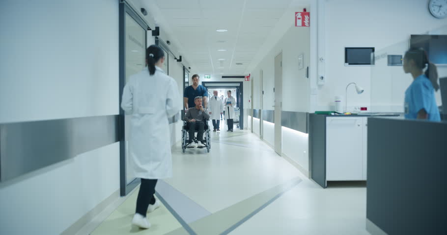 Busy Hospital Hallway with Doctors, Nurses and Specialists Preparing for the Day Ahead in Hospital. Female and Male Physicians, Surgeons, Healthcare Officials Walk Together in Corridor
