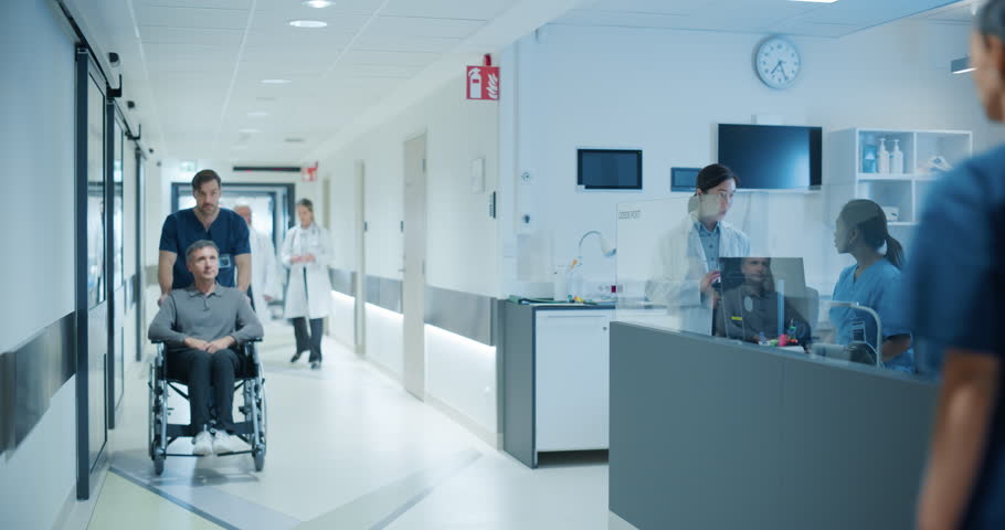 Diverse Male and Female Medical Professionals Navigate a Busy Hospital Corridor and Registration Area, Having Conversations About Healthcare. Male Nurse Assists a Patient in a Wheelchair