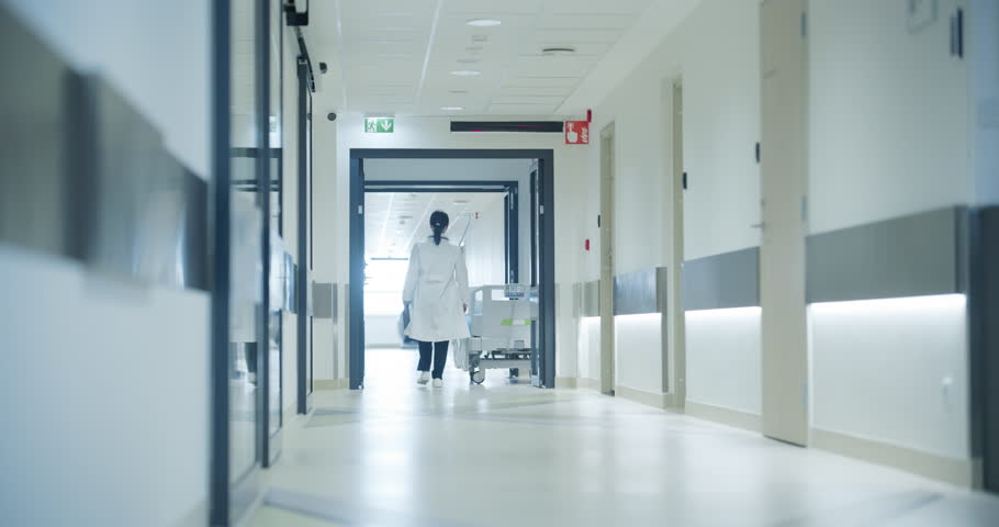 Female Doctor Walking Away in an Empty Hospital Hallway. General Practitioner Holding a Tablet Computer while Going to Intensive Care Unit or General Medicine Ward for Daily Patient Visit
