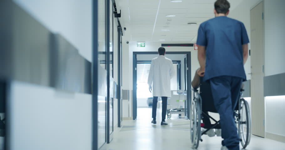 Hospital Hallway with Doctors, Nurses and Specialists in Hospital. Female and Male Physicians, Surgeons, Healthcare Officials Walk Together in Corridor with Their Back to Camera. Slow Motion Footage