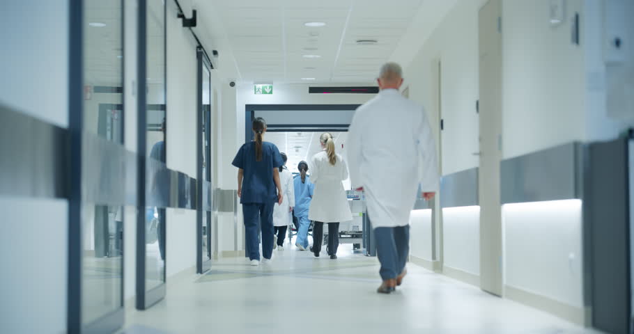 Hospital Hallway with Doctors, Nurses and Specialists in Hospital. Female and Male Physicians, Surgeons, Healthcare Officials Walk Together in Corridor with Their Back to Camera. Slow Motion Footage