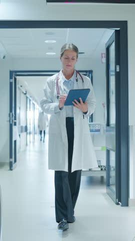 Vertical Screen: Hospital Hallway with Medical Professionals Heading to Their Designated Areas. Female Doctor Meeting Colleagues while Looking at Important Medical Details on a Tablet
