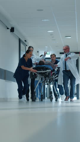 Vertical Screen: Emergency Medical Staff Moving an Injured Patient on a Stretcher Towards the Operating Room in a Hospital. Doctors, Nurses and Paramedics Taking Care a Person in Critical Condition