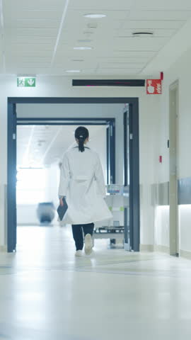 Vertical Screen: Doctor Walking Away in an Empty Hospital Hallway. General Practitioner Holding a Tablet Computer while Going to Intensive Care Unit or General Medicine Ward for Daily Patient Visit