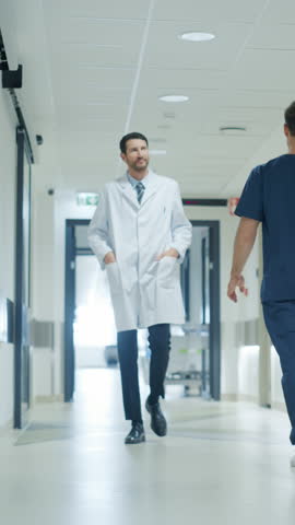 Vertical Screen: Healthcare Professionals Walking to Their Examination Rooms, Reception Desk, ICU Unit in a Hospital Corridor. Senior Doctor Inspecting Medical Information on a Tablet Computer