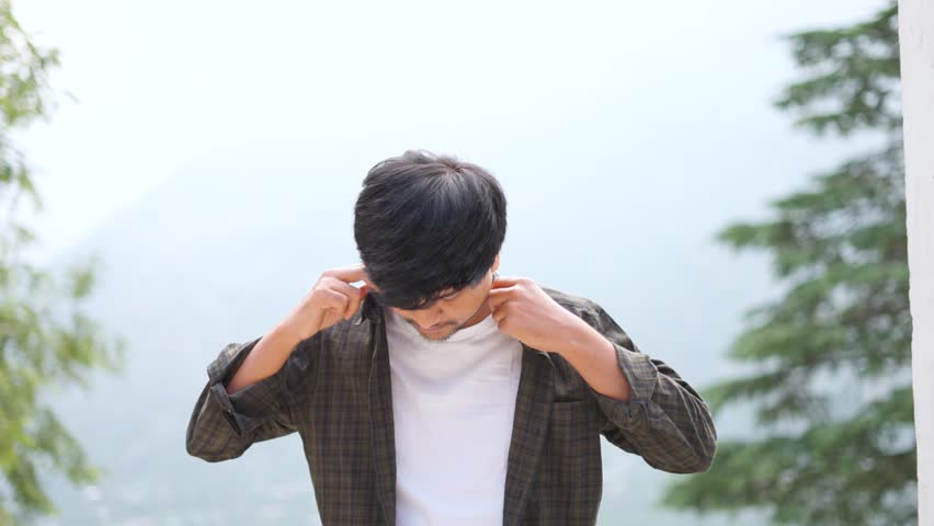 4K Portrait shot of an Indian man fixing his shirt and his clothes to look presentable while standing outside. Man in casual clothes tries to look better while meeting with someone.