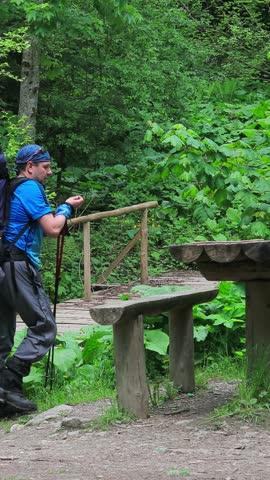 Two hikers with backpacks take a well-deserved rest at a wooden table and bench in a peaceful forest setting, enjoying the calm of nature