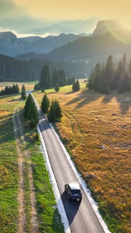 Aerial drone shot of car driving on scenic road in mountains. Flying over scenic road in the mountains with car moving along it. Vertical shot. Summer adventure by car