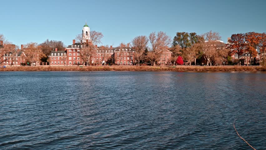 The iconic architecture of Cambridge in MA, USA showcasing the famous Charles river, the city memorable red brick buildings by Memorial Drive road and lots of locals passing by at a distance.