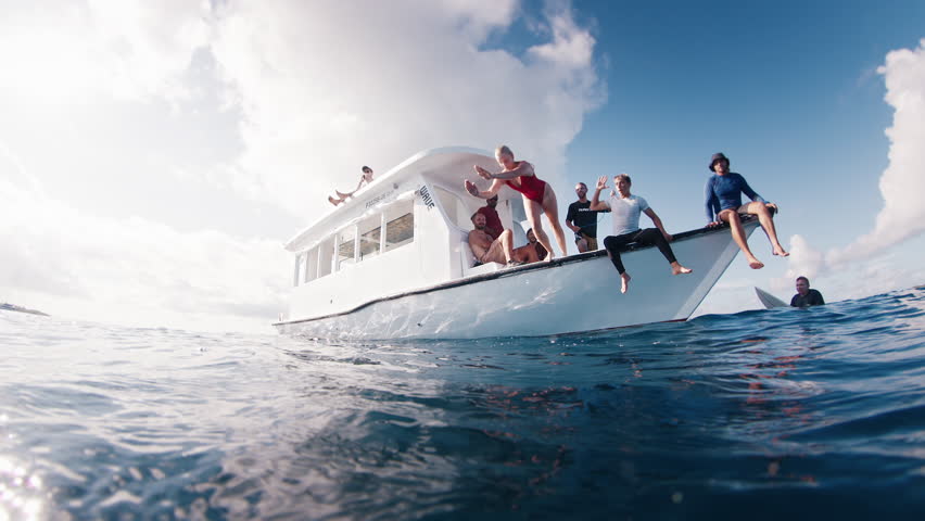 Teen girl in red suit jumps in the water from the boat and swims confidently underwater in the crystal clear tropical sea with sun shining through the water