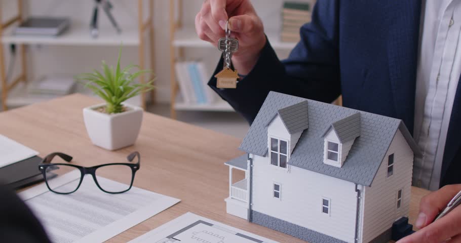 There is a model of a new house on the realtors desk, slowmotion. A broker selling an apartment gives the keys to a business man, hands close-up. Real estate investment, smart home rental