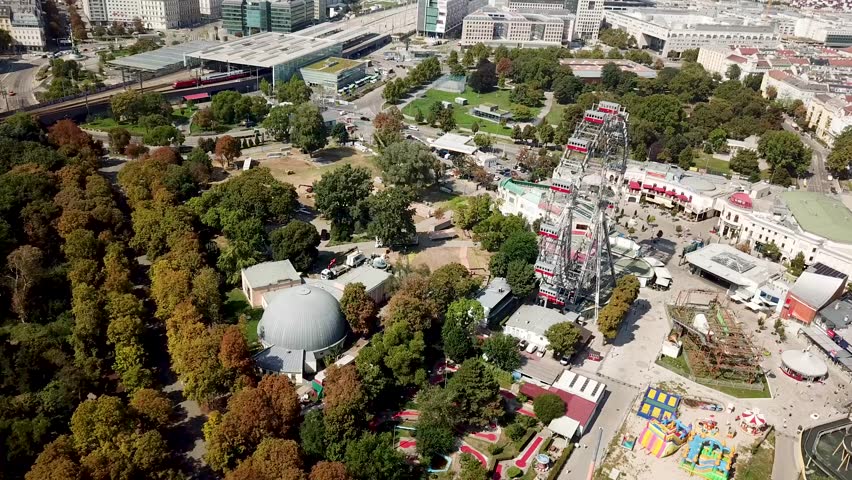 Panning Aerial shot of Worlds oldest Ferris Wheel in Vienna, Austria at Prater Amusement Park during a sunny day. Views of the city skyline with the Subway in the background.
