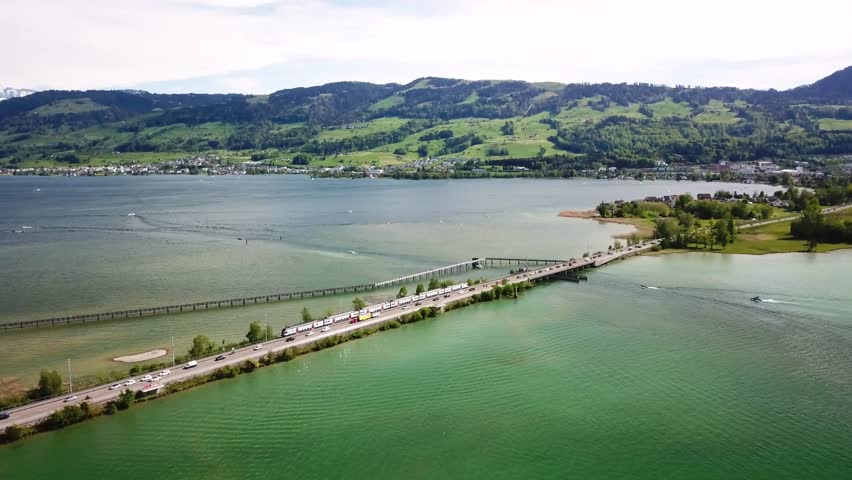 Cars traffic and train crossing causeway bridge seedamm in he upper part of lake zurich between Rapperswil and Hurden in Freienbach, Schwyz, Switzerland, drone revealing