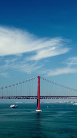 View of 25 de Abril Bridge famous tourist landmark of Lisbon connecting Lisboa to Almada on Setubal Peninsula over Tagus river with boats yachts and vessels moving. Lisbon, Portugal
